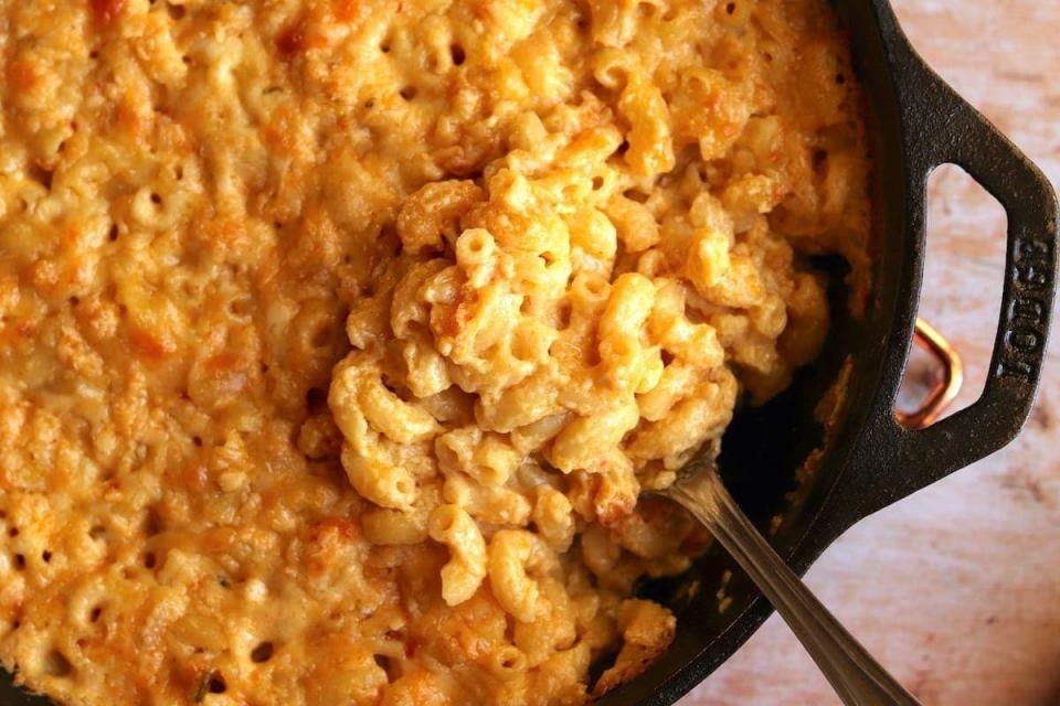 A large skillet of creamy mac 'n' cheese with a spoon scooping some of it out.