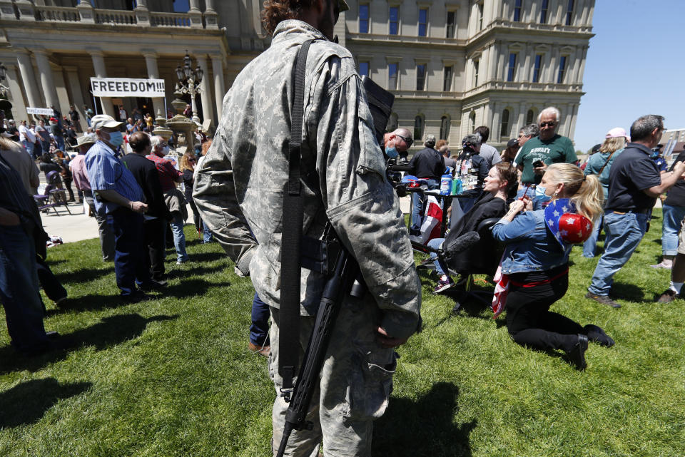 A protester with a rifle, left, watches Linda Hicks, seated, receive a free haircut from Teresa Luks, right, at the State Capitol during a rally in Lansing, Mich., Wednesday, May 20, 2020. Barbers and hair stylists are protesting the state's stay-at-home orders, a defiant demonstration that reflects how salons have become a symbol for small businesses that are eager to reopen two months after the COVID-19 pandemic began. (AP Photo/Paul Sancya)