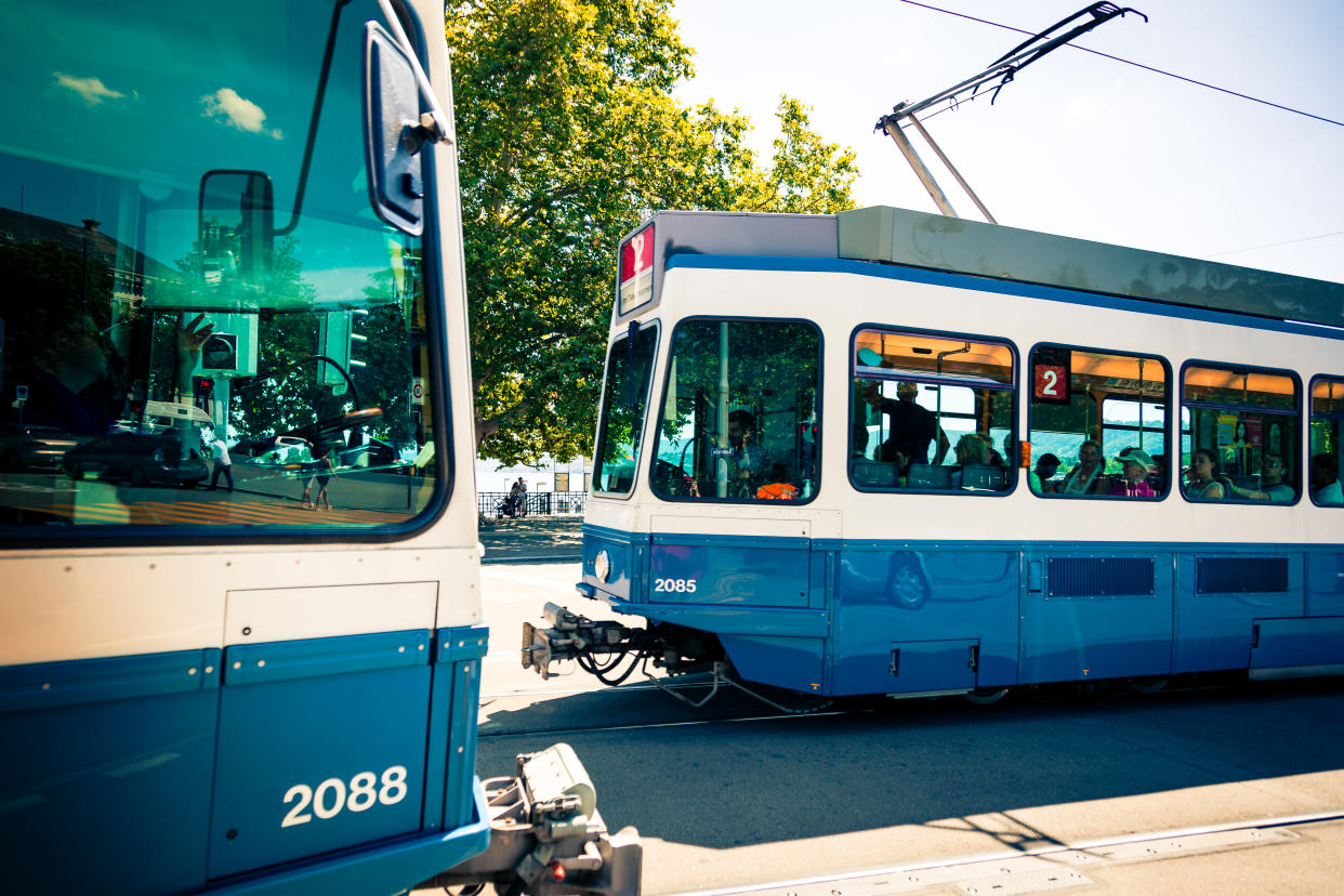 Color image depicting two trams filled with people on the streets of downtown Zurich, Switzerland. Room for copy space.