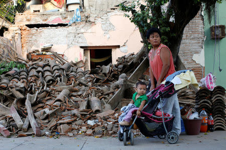 A woman with a baby stands next to a house which was damaged in an earthquake that struck the southern coast of Mexico late on Thursday, in Juchitan, Mexico, September 9, 2017. REUTERS/Carlos Jasso