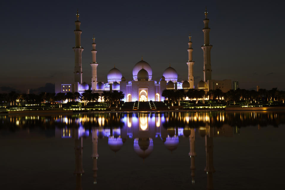 The Sheikh Zayed Grand Mosque is seen with its lights on at dusk in Abu Dhabi, United Arab Emirates, Wednesday, Dec. 9, 2020. Abu Dhabi announced Wednesday it would resume "all economic, tourism, cultural and entertainment activities in the emirate within two weeks." It attributed the decision to "successes" in halting the spread of the coronavirus. (AP Photo/Jon Gambrell)