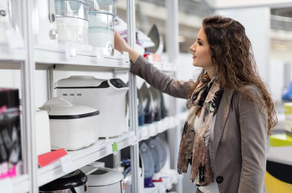 A person smiles while shopping for various home cooking equipment and appliances in a store. 