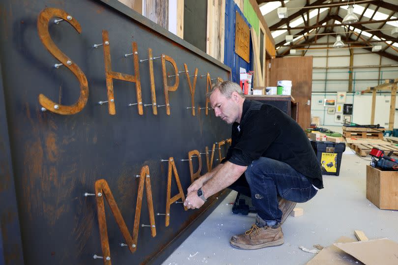 Alec Short tightens the letters on the sign for the new Shipyard Market in Porthleven