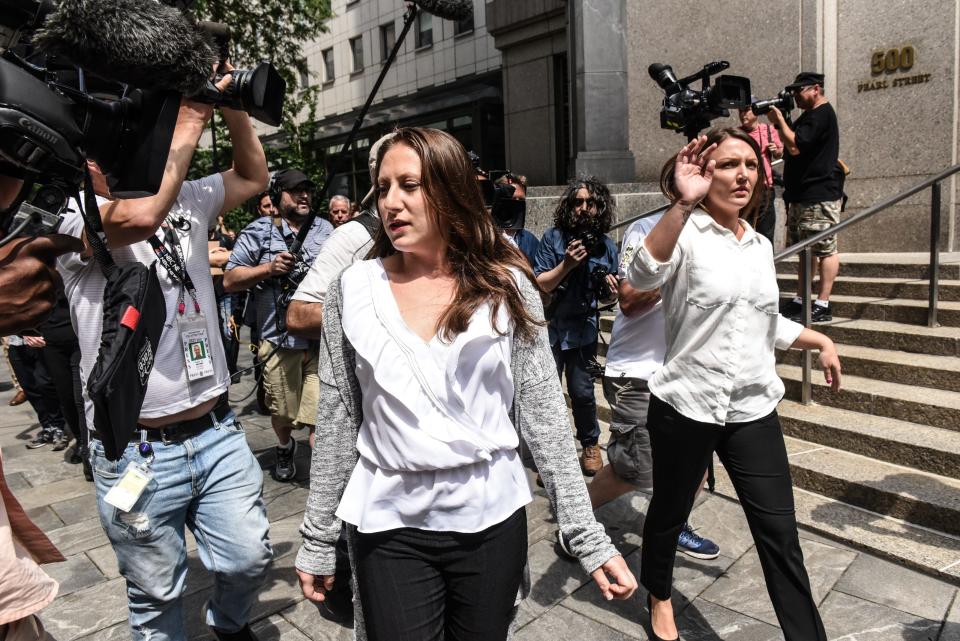 Two women are seen walking ahead by a building as they're followed by news photographers.