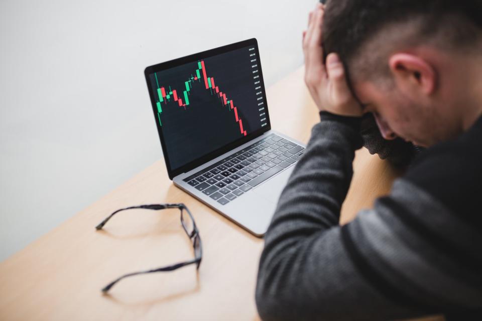 A person has their head in their hands while looking at a stock chart going down. 