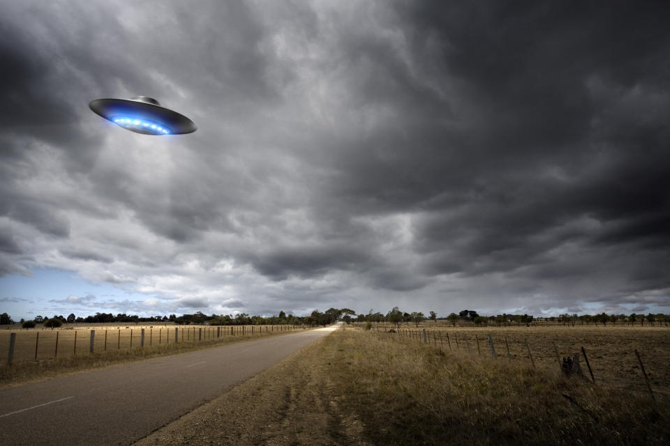 a ufo hovering over a small country road