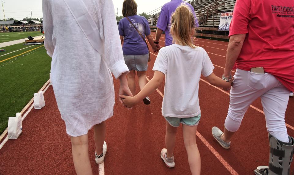 Participants link hands as they walk around the track at Erhard Field during the Relay for Life ceremony.