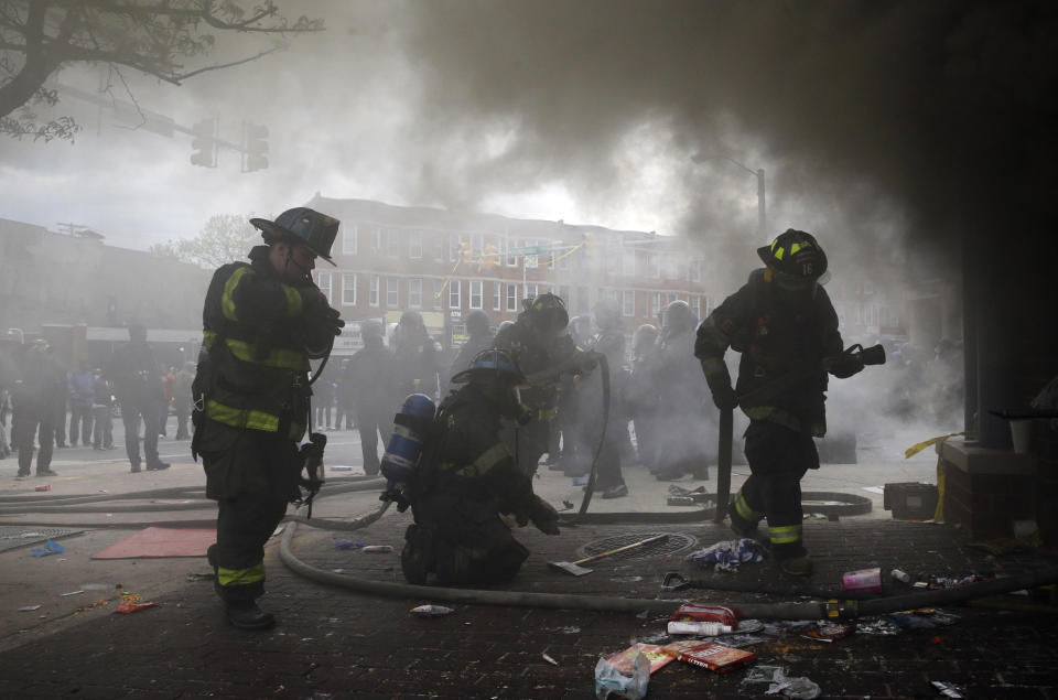 Firefighters prepare to put out a fire at a store, Monday, April 27, 2015, during unrest following the funeral of Freddie Gray in Baltimore. Gray died from spinal injuries about a week after he was arrested and transported in a Baltimore Police Department van. (AP Photo/Patrick Semansky)