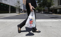 FILE - A woman walks with a plastic bag in Sacramento, Calif., on Wednesday, May 14, 2014. California in 2014 enacted the nation's first ban on single-use plastic shopping bags. But in 2022, state Attorney General Rob Bonta says consumers who think they're helping the environment with reusable plastic bags had better think again. He says manufacturers can't back up their claim that the thicker, more durable bags are recyclable in California. (AP Photo, File)