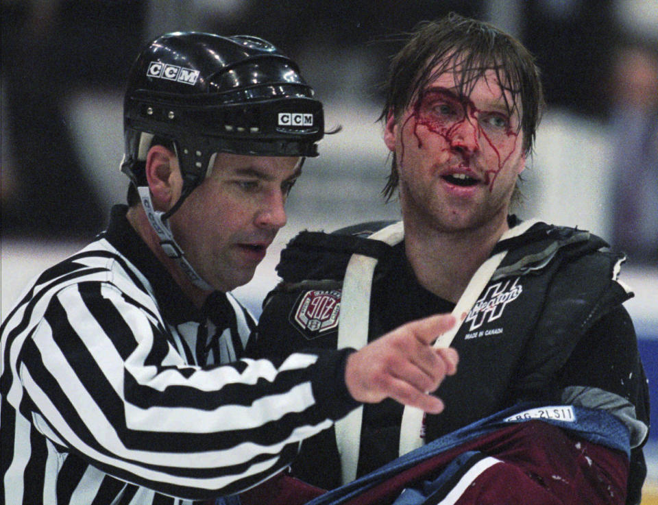FILE - Linesman Dan Schachte, left, leads a bleeding Colorado Avalanche goaltender Patrick Roy to his bench after Roy was involved in a first-period brawl with Detroit Red Wings' goaltender Mike Vernon in Detroit, March 26, 1997. The league rule changes have made it so punitive that goalie fighting has essentially disappeared from the highest level of hockey. (AP Photo/Tom Pidgeon, File)