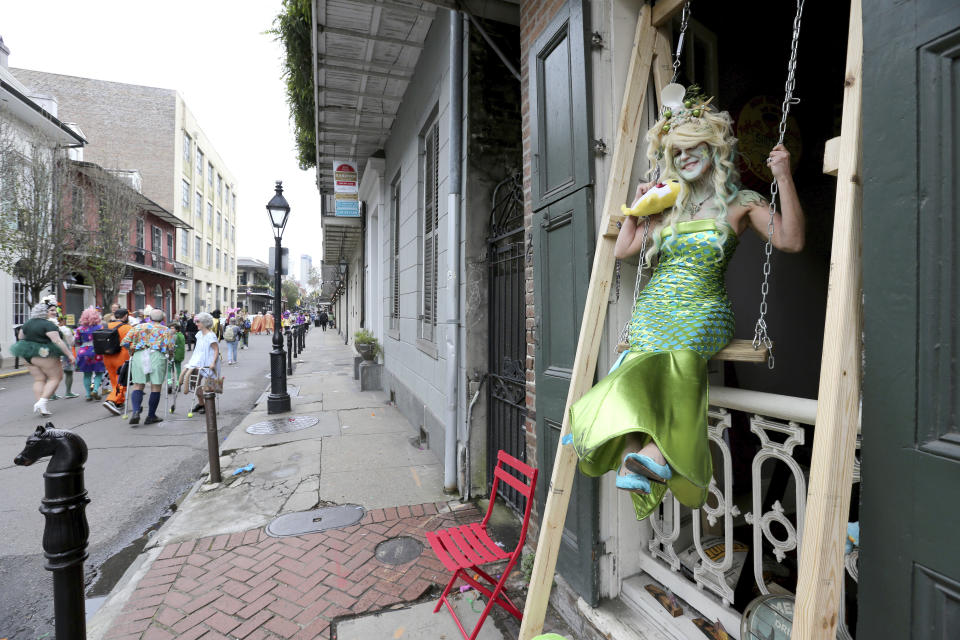 Laura Kamenitz, dressed as a mermaid, swings in the window of her apartment as revelers pass on Chartres Street in New Orleans, Tuesday, Feb. 25, 2020. (AP Photo/Rusty Costanza)