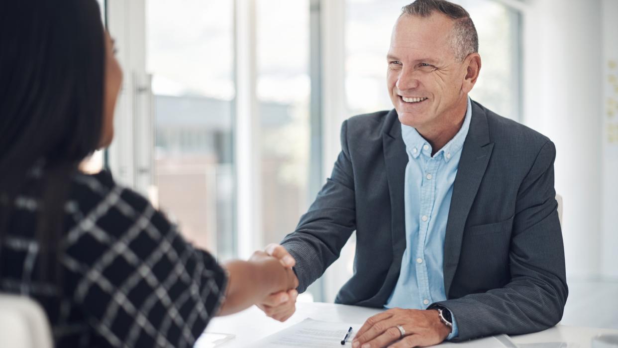  Photo of a man shaking hands with someone behind a desk after doing business in a modern office. 