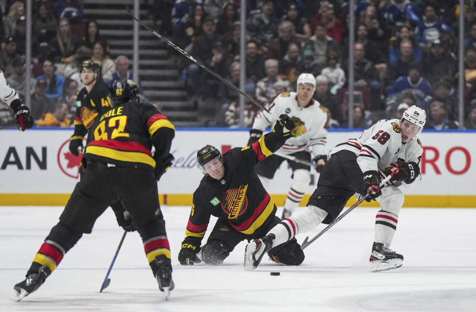 Chicago Blackhawks' MacKenzie Entwistle, right, reaches for the puck after colliding with Vancouver Canucks' Brock Boeser, center, during the third period of an NHL hockey game in Vancouver, British Columbia, on Monday, Jan. 22, 2024. (Darryl Dyck/The Canadian Press via AP)
