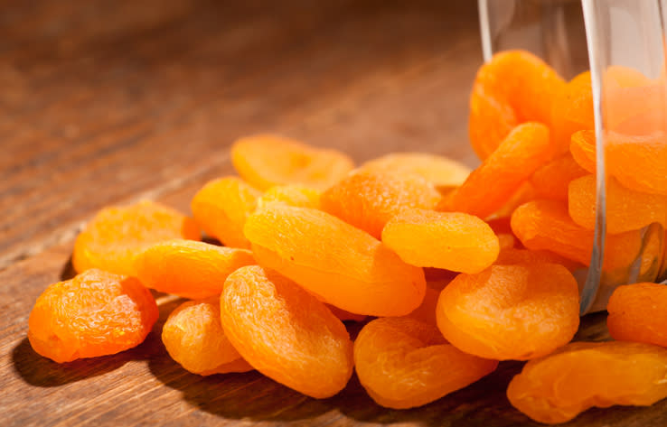 Dried apricots spill from a transparent jar onto a wooden surface