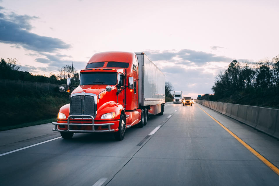 Orange red 18 wheeler new semi truck delivering goods on the road at night with headlights