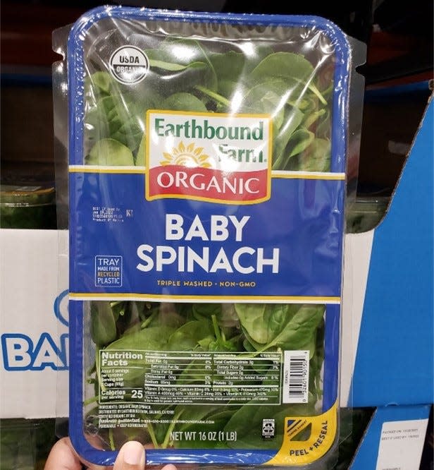 Hand holding blue pack of baby spinach at costco