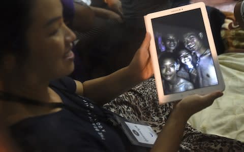 A happy family member shows the latest pictures of the missing boys taken by rescue divers inside the cave - Credit: Lillian Suwanrumpha/AFP