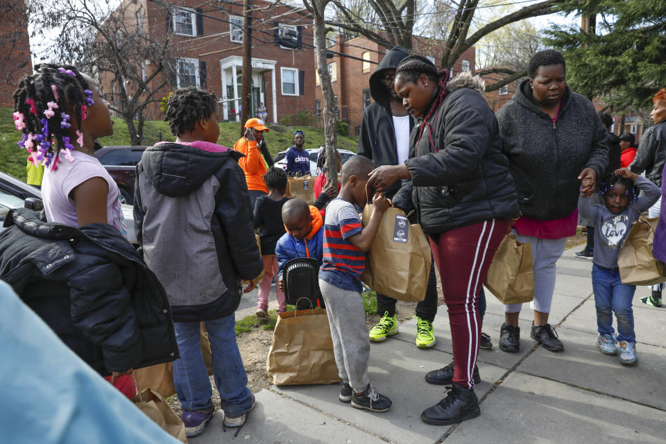 In this March 29, 2020, photo, Kahlil Middleton, 5, center, looks inside a bag containing a hot meal held by his mother, Alexis Whitley, near their apartment in southeast Washington. Whitley worked at Nationals Stadium but was laid off as a result of the coronavirus closures. Neighborhood deliveries are part of a new Martha's Table initiative, along with community partners, to get needed food directly to the neighborhoods that they serve. (AP Photo/Jacquelyn Martin)