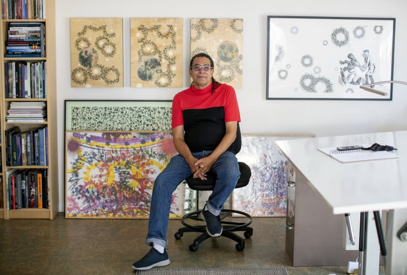 Painter Mark Steven Greenfield sits amid detailed paintings and a drafting table in his studio