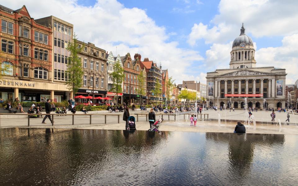 Various people sitting, walking, visiting in the main Market Square, Nottingham Council House building behind.