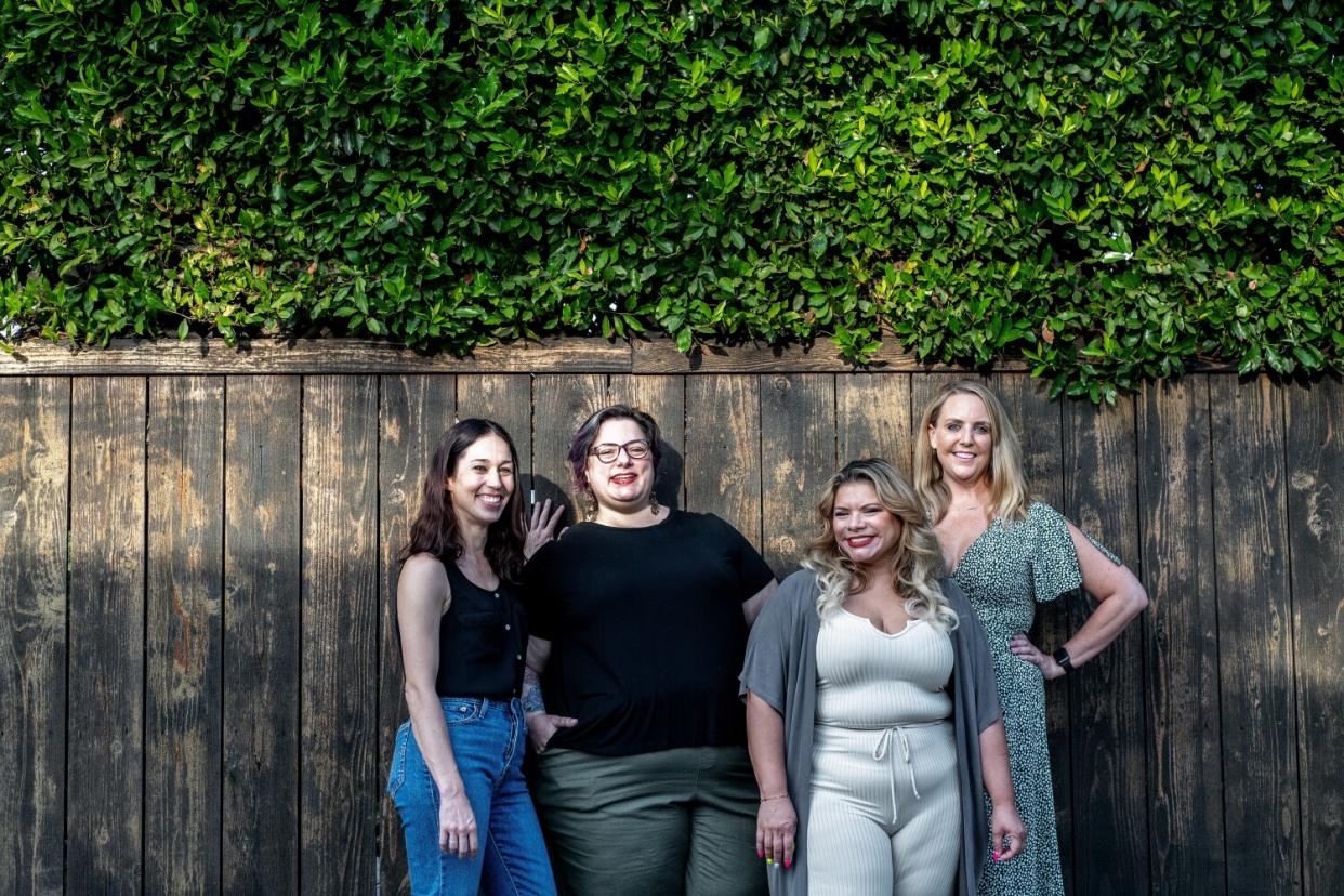 Four women stand together in front of a wooden fence.