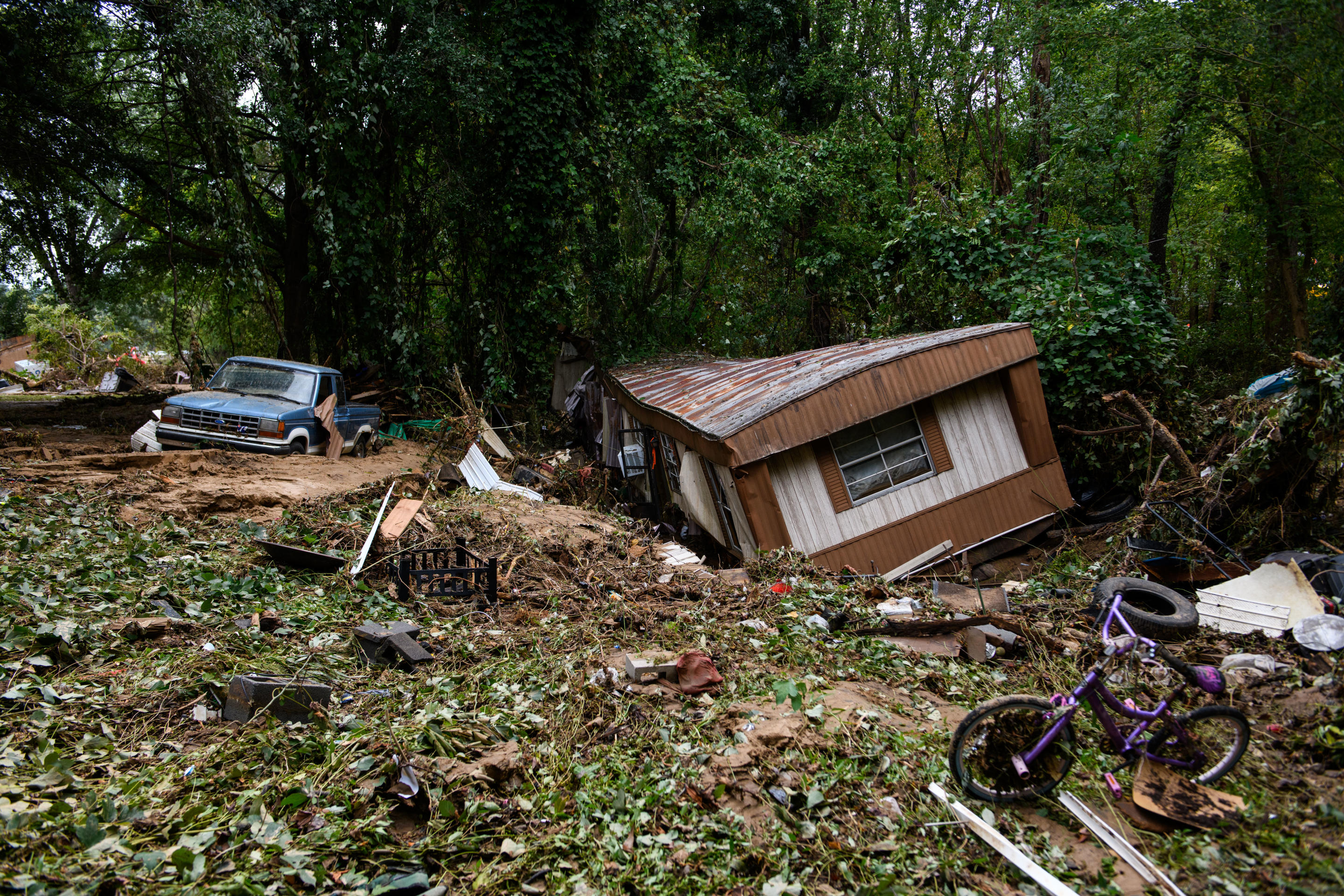 A crumpled RV, a child's bicycle, a pickup truck and other debris are visible along a treeline in Old Fort, NC