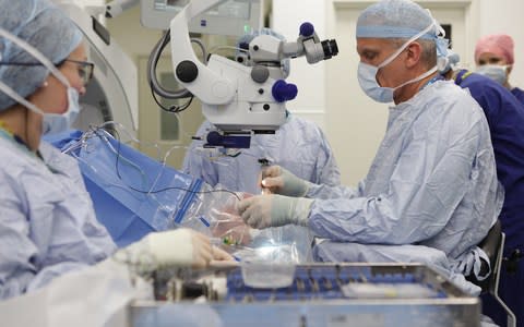 Prof Robert MacLaren, right, injects the virus into the eye of Janet Osborne