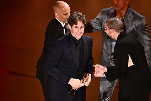 <p>PATRICK T. FALLON/AFP via Getty Images</p> Jonathan Glazer (center) accepts the award for Best International Feature at the Oscars in Los Angeles on March 10, 2024