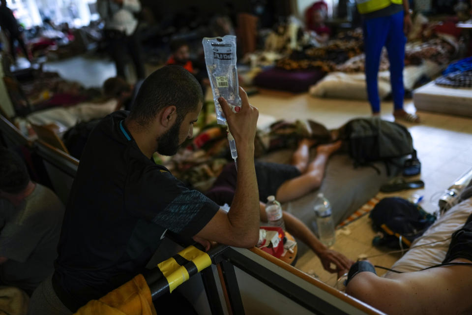 A man on hunger strike holds up a saline drip while his comrade is prepared to be transferred to a hospital as they occupy a big room of the ULB French university in Brussels, Tuesday, June 29, 2021. More than two hundreds of migrants without official papers and who have been occupying a church and two buildings of two Brussels universities since last February, began a hunger strike on 23 May to draw the attention of Brussels authorities to their plight. (AP Photo/Francisco Seco)