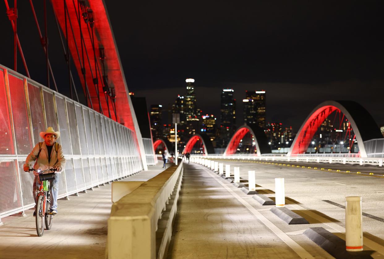 A cyclist crossing the Sixth Street Viaduct at night which has been illuminated with red lights.