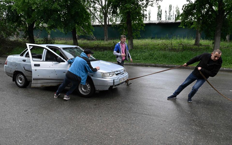 Local residents try to tow a damaged car in the Saltivka district, northern Kharkiv - GENYA SAVILOV /AFP