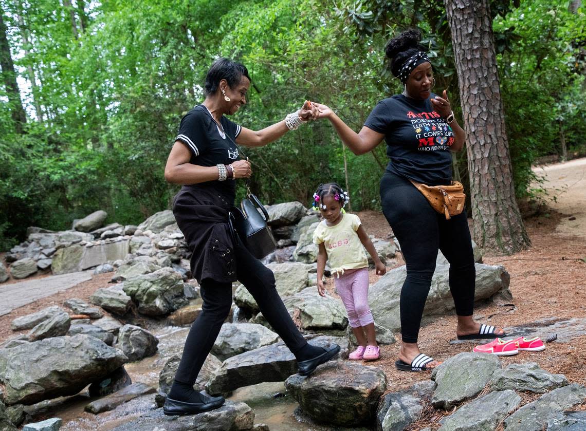 Brenda Vann is helped across a stream by her daughter, LaTasha McNeil, as her granddaughter, Jayla Brown, 3, watches at the Museum of Life and Science in Durham, N.C. on Tuesday, May 3, 2022.