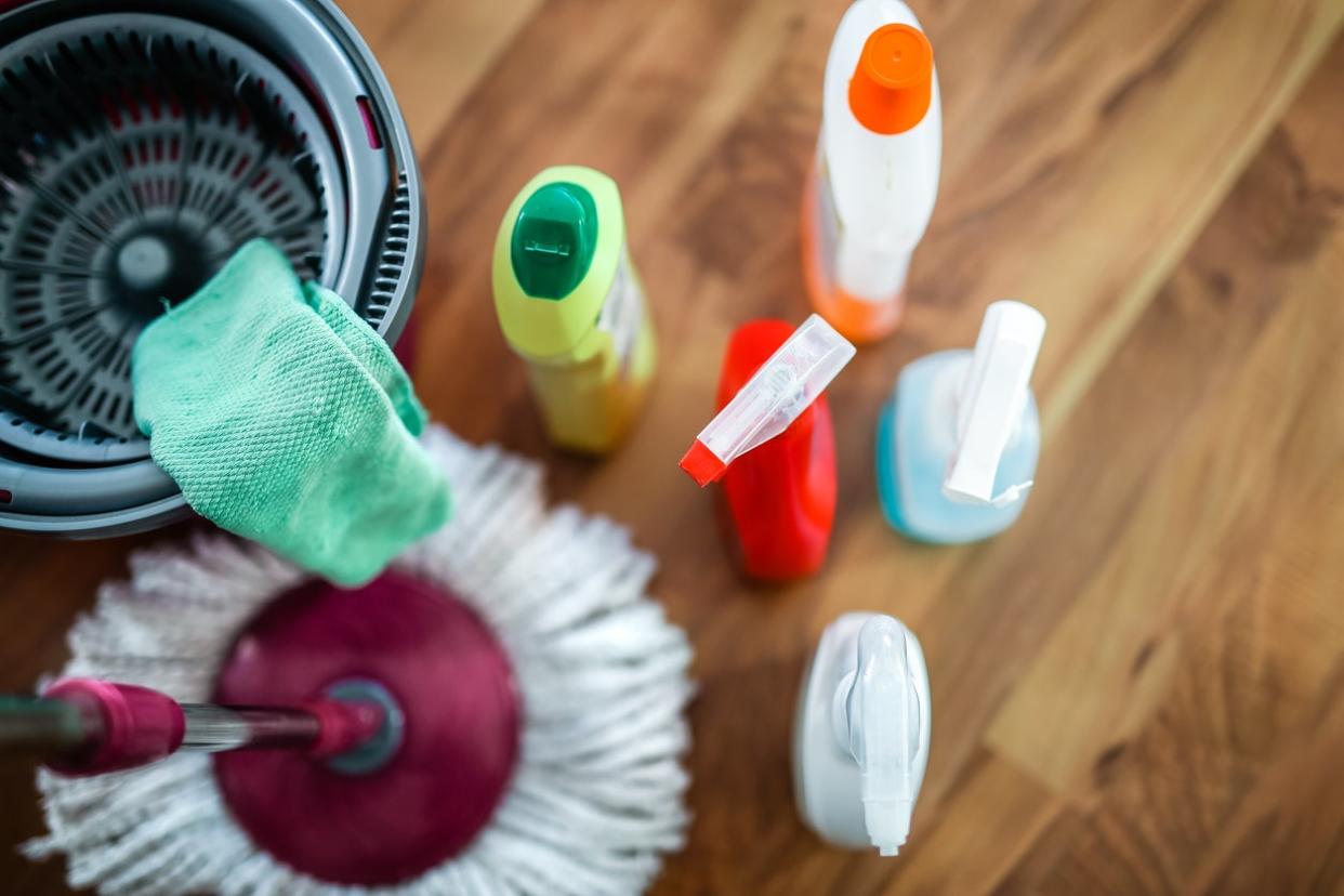 overhead view of cleaning products in spray bottles and capped bottles with mop and bucket on wood floor