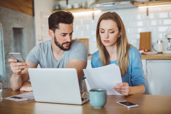 A couple with a laptop, smartphones, papers, and coffee set up as they plan their household finances. 