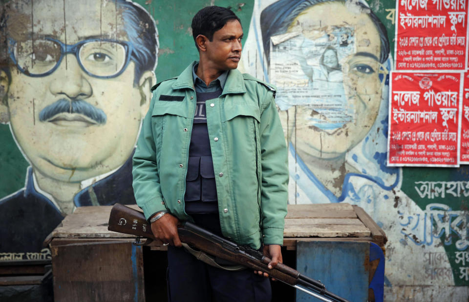 FILE- A Bangladeshi armed policeman stands guard in front of a mural of Bangladesh's Prime Minister Sheikh Hasina and her father and founder of the nation Sheikh Mujibur Rahman in Dhaka, Bangladesh, Jan. 8, 2014. Prime Minister Hasina's political life was shaped by the Aug. 15, 1975 military coup and assassination of her father, Rahman, the first leader of independent Bangladesh. Some say the brutal takeover, which also killed most of her family, pushed her to consolidate unprecedented power. (AP Photo/Rajesh Kumar Singh, File)