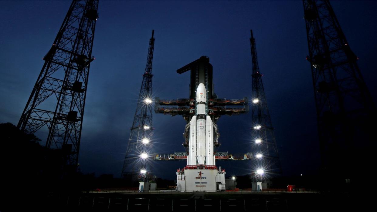  a white rocket stands on its launch pad against a blue-black sky 