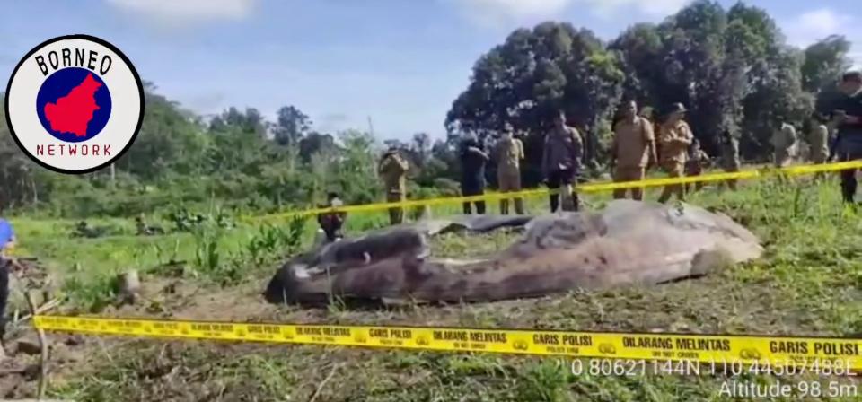 large rounded metal sheet in a field surrounded by yellow tape and a handful of people