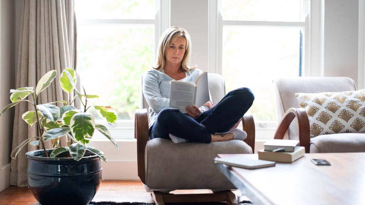 Full length of mature woman reading book on chair.