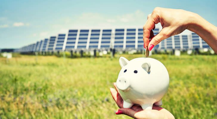 Solar penny stocks: Piggy bank in front of solar panel infrastructure