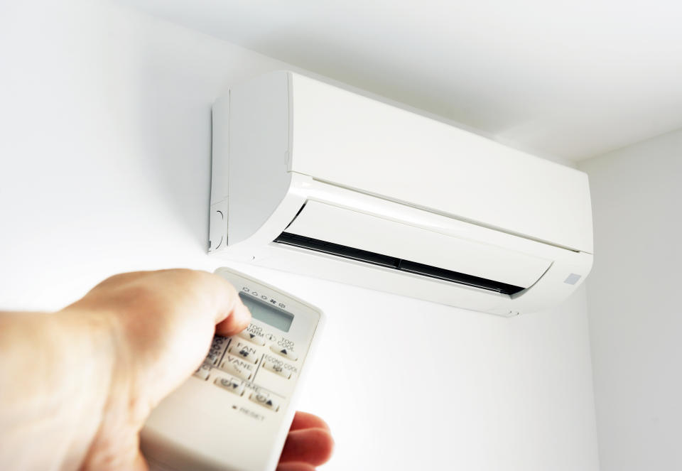 Hand holding a remote control targeting a wall-mounted air conditioning unit, illustrating a modern office or home cooling system