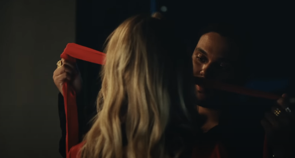 The Weeknd's character holds a blindfold up to a female character