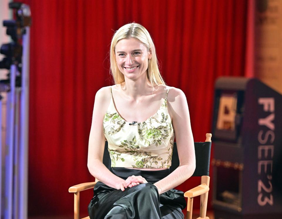 Elizabeth Debicki sitting in a director's chair with her legs crossed and her hands together