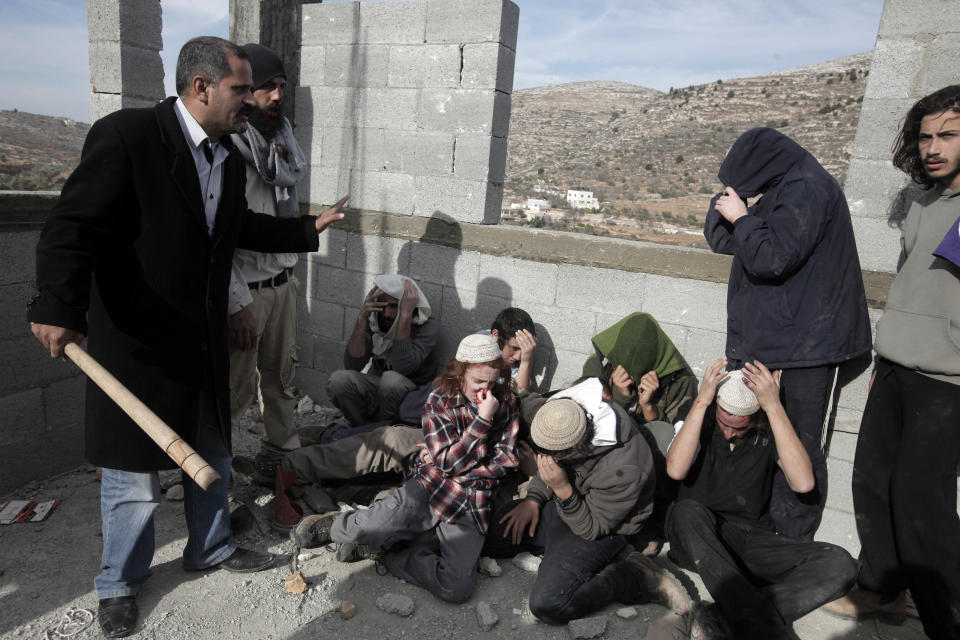 A Palestinian man (L) from the village of Qusra protects a group of Israeli settlers after Palestinians detained and beat them at a construction site in the Israeli occupied West Bank, on January 7, 2014. (JAAFAR ASHTIYEH/AFP/Getty Images)