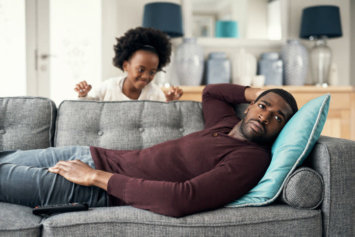 A little girl trying to get her dad's attention as he looks at the TV