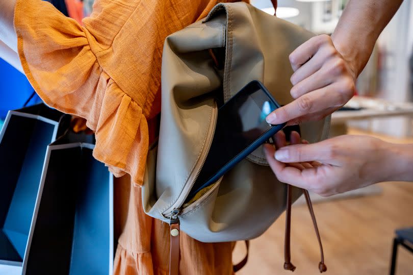 Close up shot of female thief trying to steal a smartphone while customer is looking at clothes in a store - Criminal lifestyles