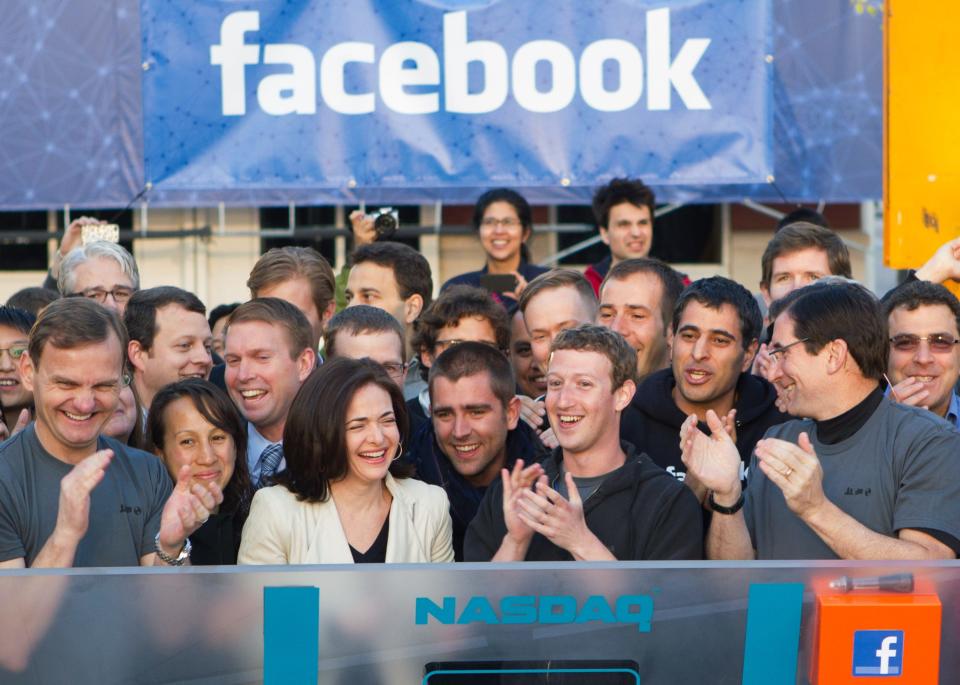A group of people, with Mark Zuckerberg in front, applauds behind a "NASDAQ" sign