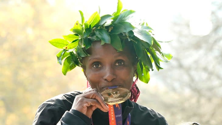 A woman kisses a medal with a green laurel on her head. 