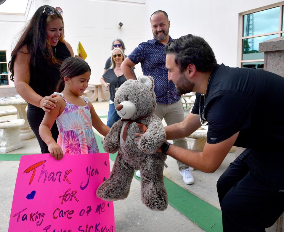 Kiali Vazquez Rodriguez, 6, with her parents, Monica Rodriguez, left, and Ricardo Vazquez, center, receives a large teddy bear from Dr. Fernando Rivera Alvarez, right, Monday at HCA Florida Sarasota Doctors Hospital.  In late, August, Kiali had a severe asthma attack triggered by COVID-19.  Her family wanted to thank the doctors and nurses and arranged a reunion. 