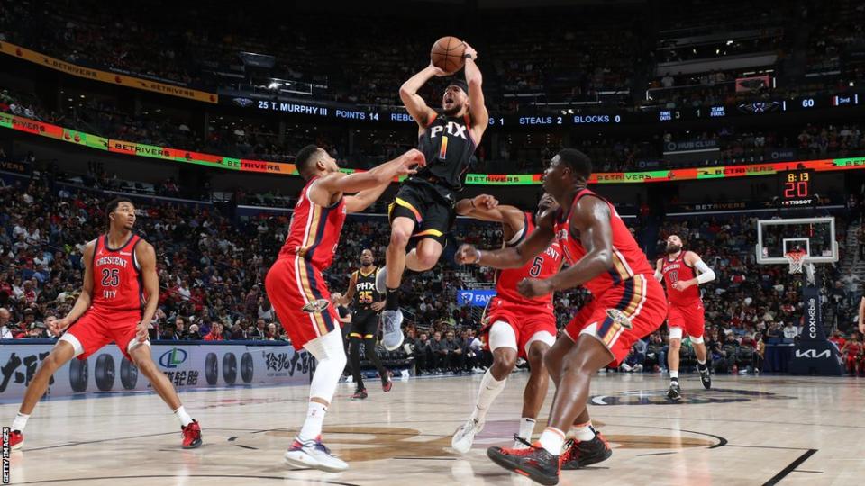 Devin Booker jumping for a basket above three New Orleans players