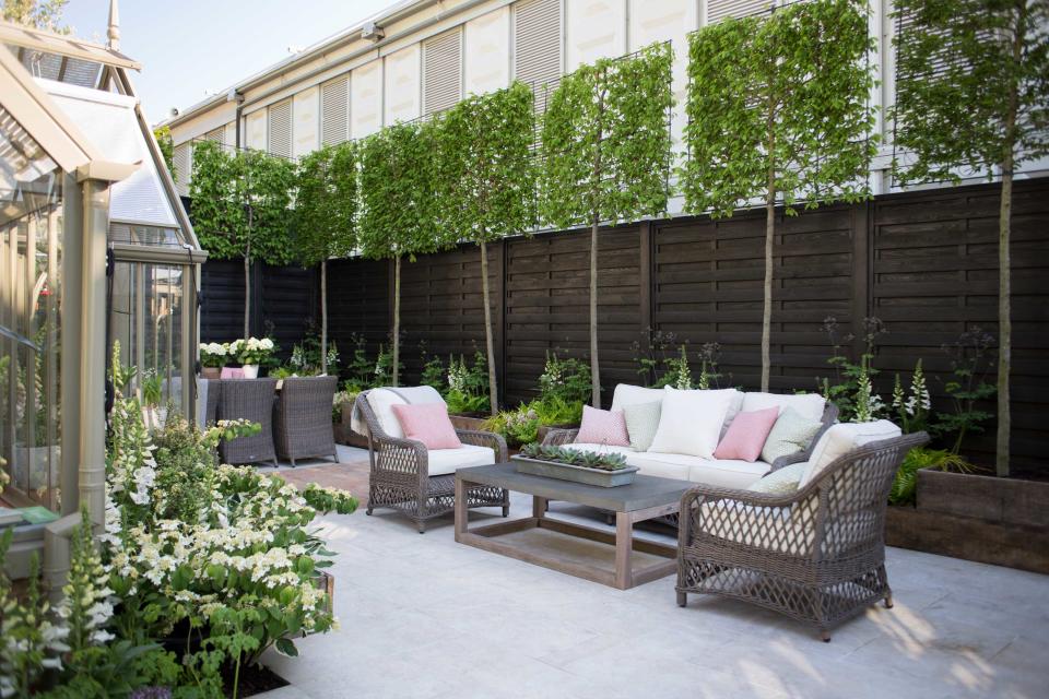 <p> This sturdy black fence is a perfect choice for chic urban living. Painted in dark tones, it feels effortlessly cool. </p> <p> A neat row of espaliered trees adds an extra level of privacy up top, and brings a fresh pop of green against the dark hue. Further planting below continues to lift the zone, adding to the welcoming vibe. </p> <p> Pale tones tie together the rest of the space, offering a striking contrast to the surrounding screen. Meanwhile, a scattering of cushions provides an accent of pink – a playful finishing flourish. </p>